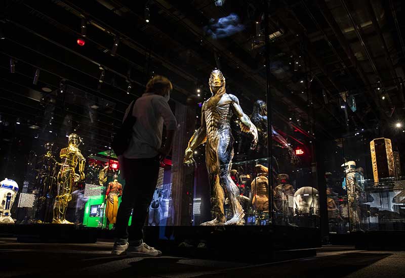 A man observing a showcase of Star Wars costumes, featuring various characters from the iconic franchise.